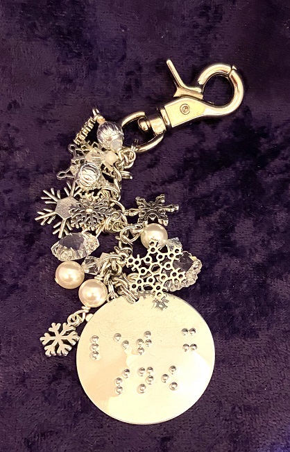 This is our brand new Sparkling Snowfall purse charm. It is lying on a purple background.