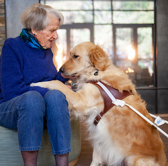 A woman sits next to a Golden Retriever guide dog; the dog has a paw in the woman's lap.