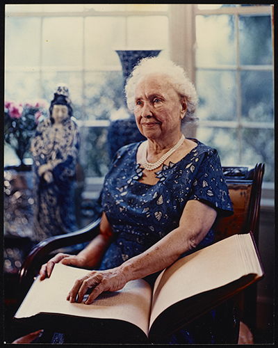 Helen Keller seated at her home in Westport, CT. She is reading a book in braille.