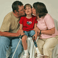 Portrait of parents kissing daughter?s cheeks. Little girl is holding a white cane and has a prosthetic leg
