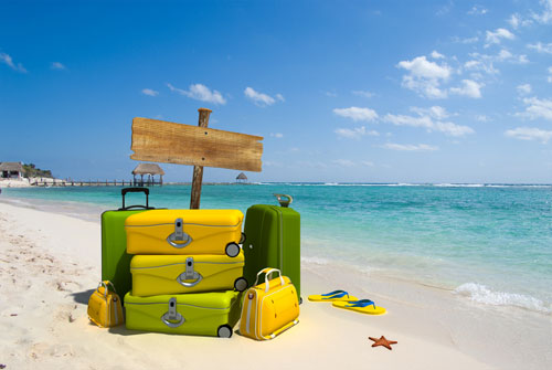 Pile of yellow luggage on a resort beach with a blank wooden sign post