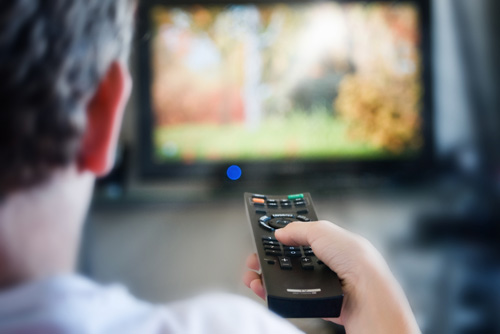 A boy's hand aims a remote control towards the television. 