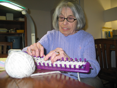 Chralotte Schrier, working on a handheld loom under a task light