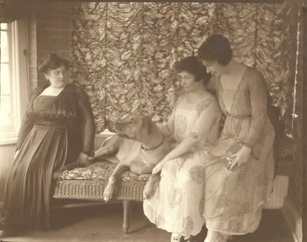 この写真は、1918 年頃、ニューヨーク州フォレスト ヒルズの自宅で籐のソファに座っているアン、犬のジークレンデ、ヘレン、ポリーを左から右に示しています。アンは窓の一番近くに座っています。 ジークレンデは彼女の隣のソファに座り、ヘレンにもたれかかる。 ヘレンは右腕をジークレンデに回している。