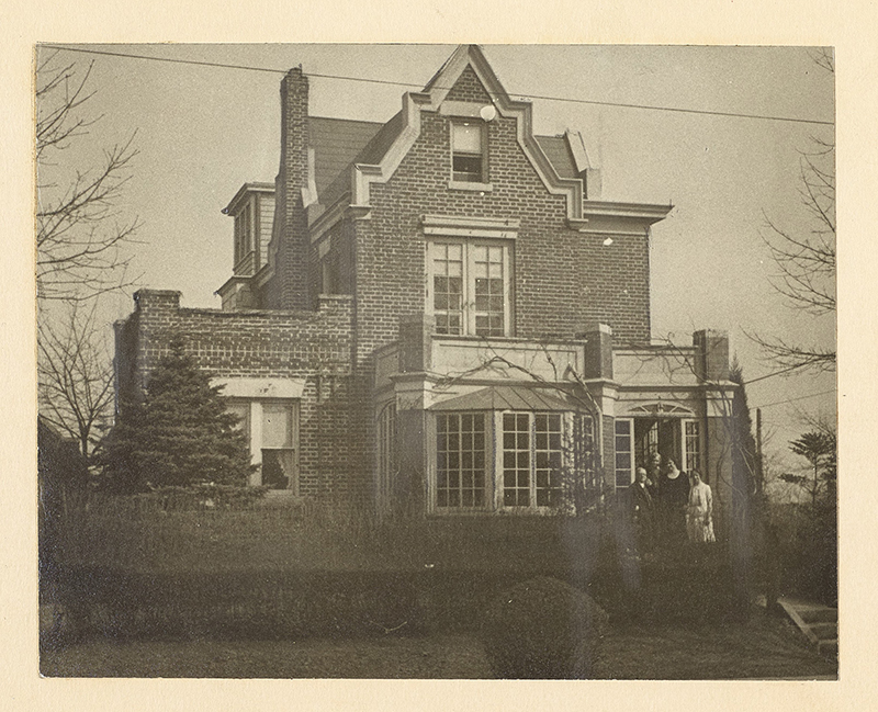 Exterior view of Helen Keller home in Forest Hills, Queens.The 2-story brick home has castle-like decorative turrets. Walter Holmes (?), Anne Sullivan Macy, Helen Keller, and Polly Thomson stand at an open door.