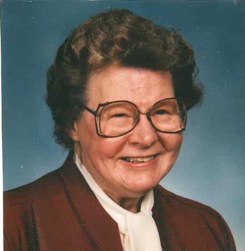 Head shot of Ruth Stank. She is middle-aged and has glasses. She is wearing a rust-colored jacket over a white blouse.