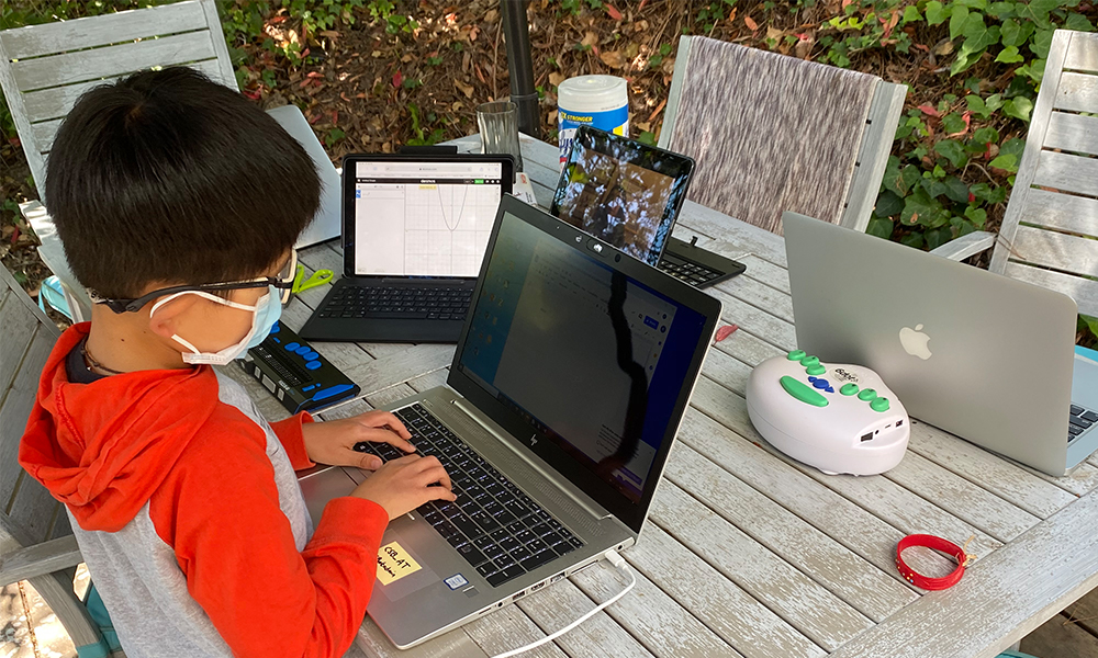 Student working outside on his laptop, wearing a mask.