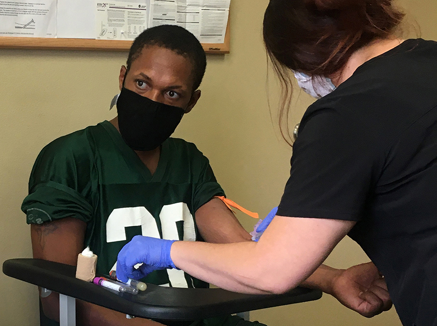 A Black man wearing a mask has blood taken for a medical test.