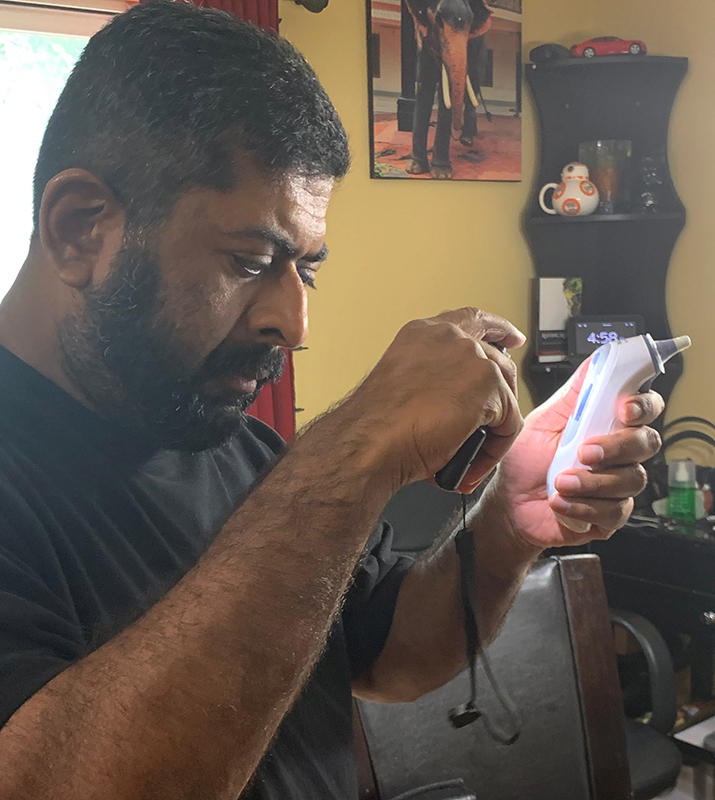 A middle-aged Indian man uses his smartphone to read the print on a thermometer. 