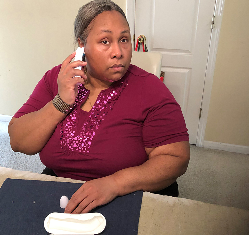 A middle-aged Black woman holds an accessible thermometer up to her ear to take her temperature.