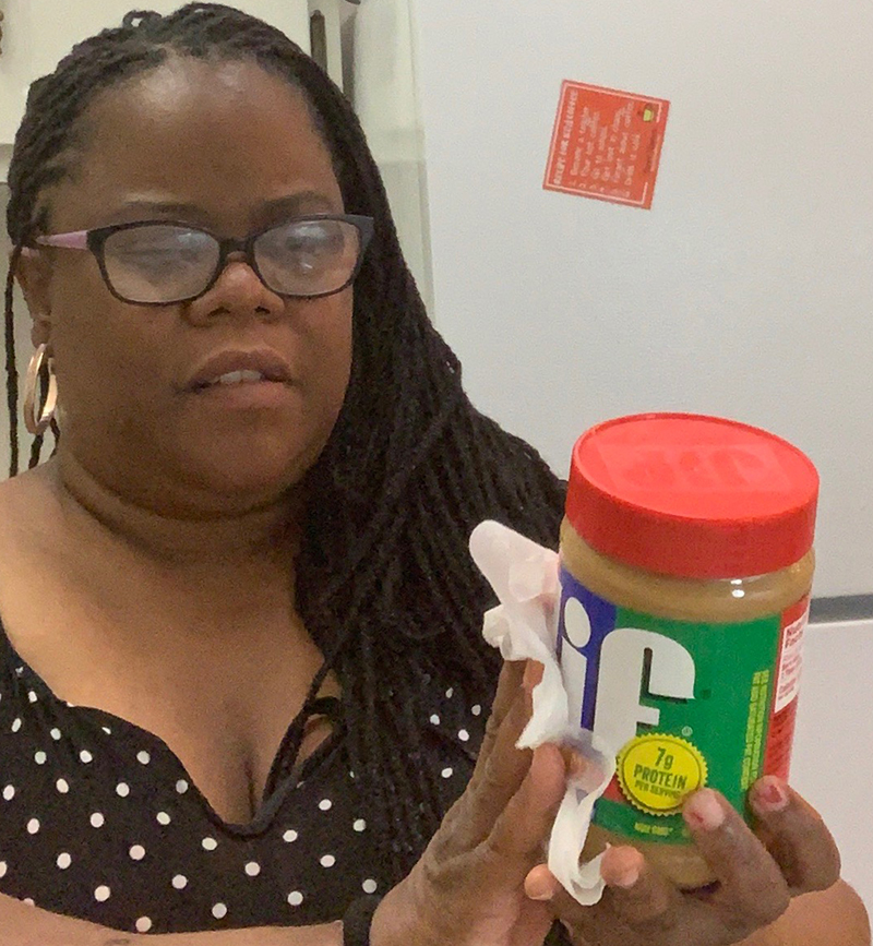 A young Black woman uses a wipe to disinfect a jar of peanut butter.