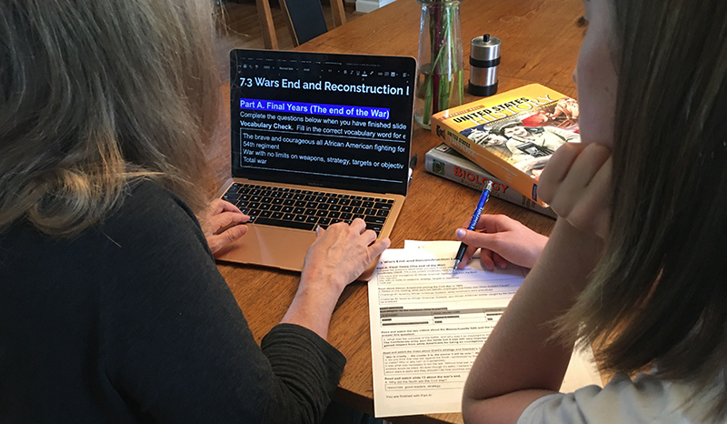 A White woman views enlarged text on a laptop, and a teenage girl next to her has the same information on a print worksheet.
