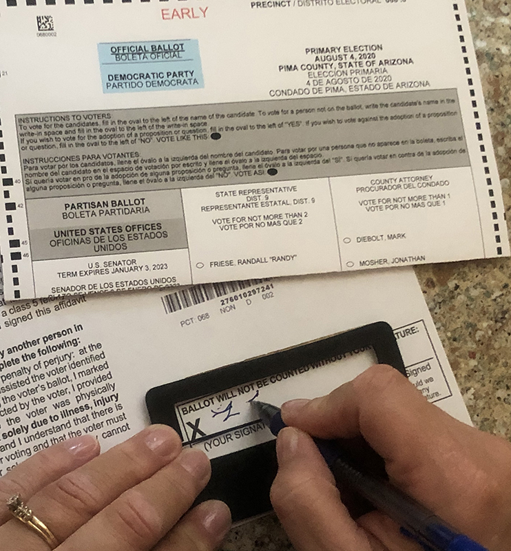 A White woman uses a signature guide to sign a paper ballot.