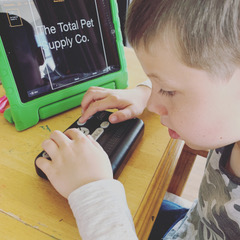 A White school-age boy uses a braille notetaker with an iPad displaying large print.