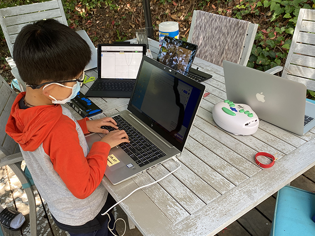 An Asian school-age boy wearing a mask types on a laptop computer. He is learning to touch type.