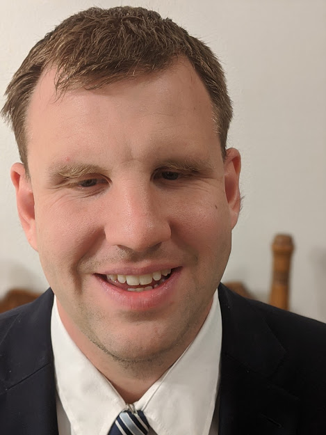 Skylar Covich headshot. A man wearing a suit and tie, smiling.