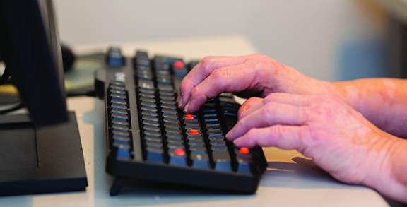 A close view of fair skinned hands on a keyboard with large raised dots on several keys