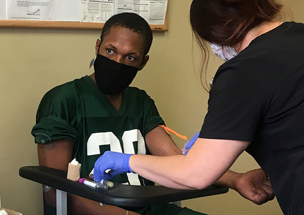 A Black man wearing a mask has blood taken for a medical test.