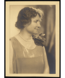 Helen Keller three-quarter profile view. She is wearing a pearl necklace and a boutonniere.. 