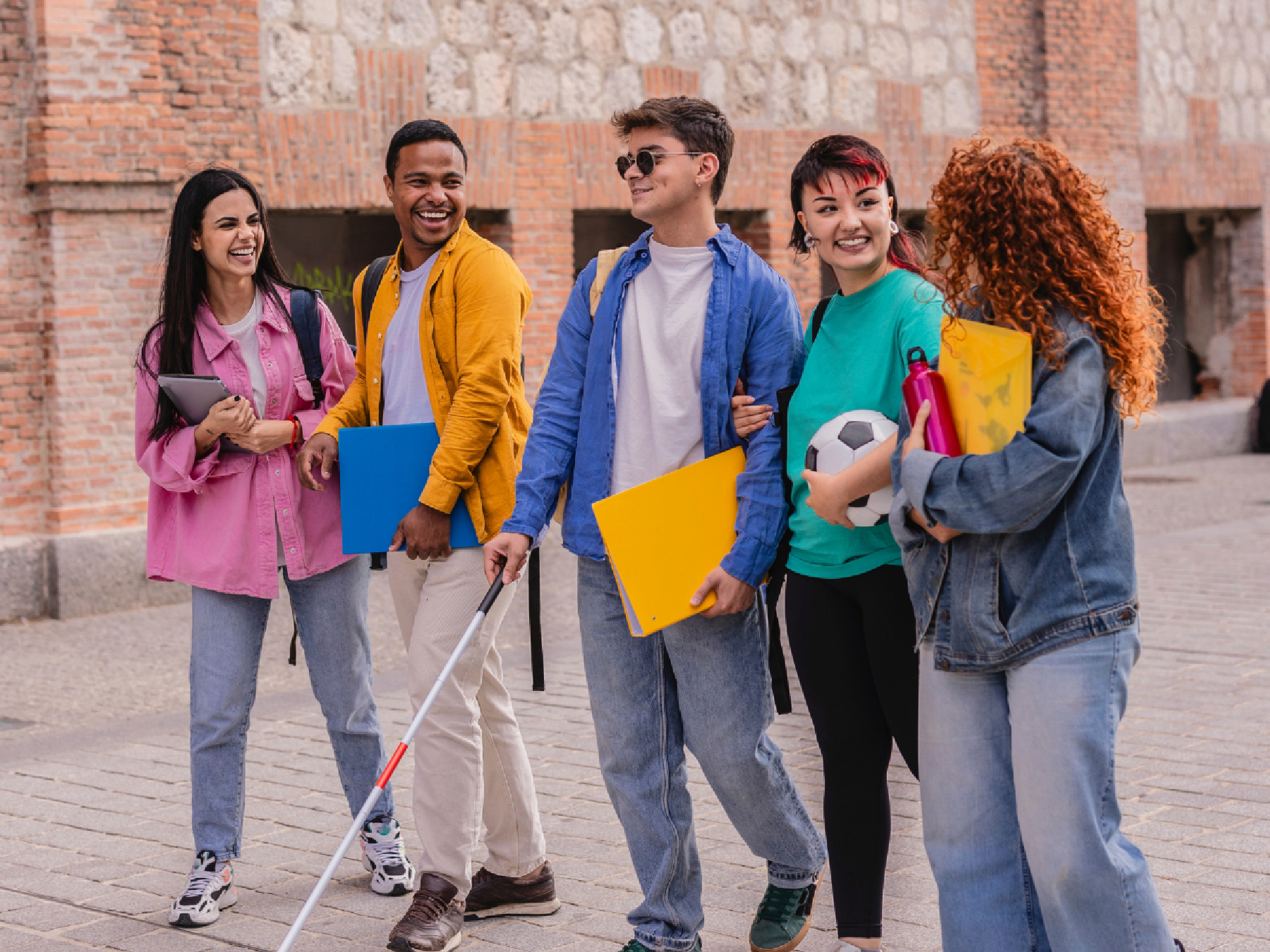 A student with a white cane smiles as he walks with his group of friends.