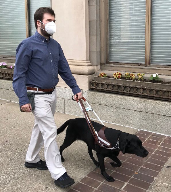 Young white man wearing a mask and walking with a guide dog.