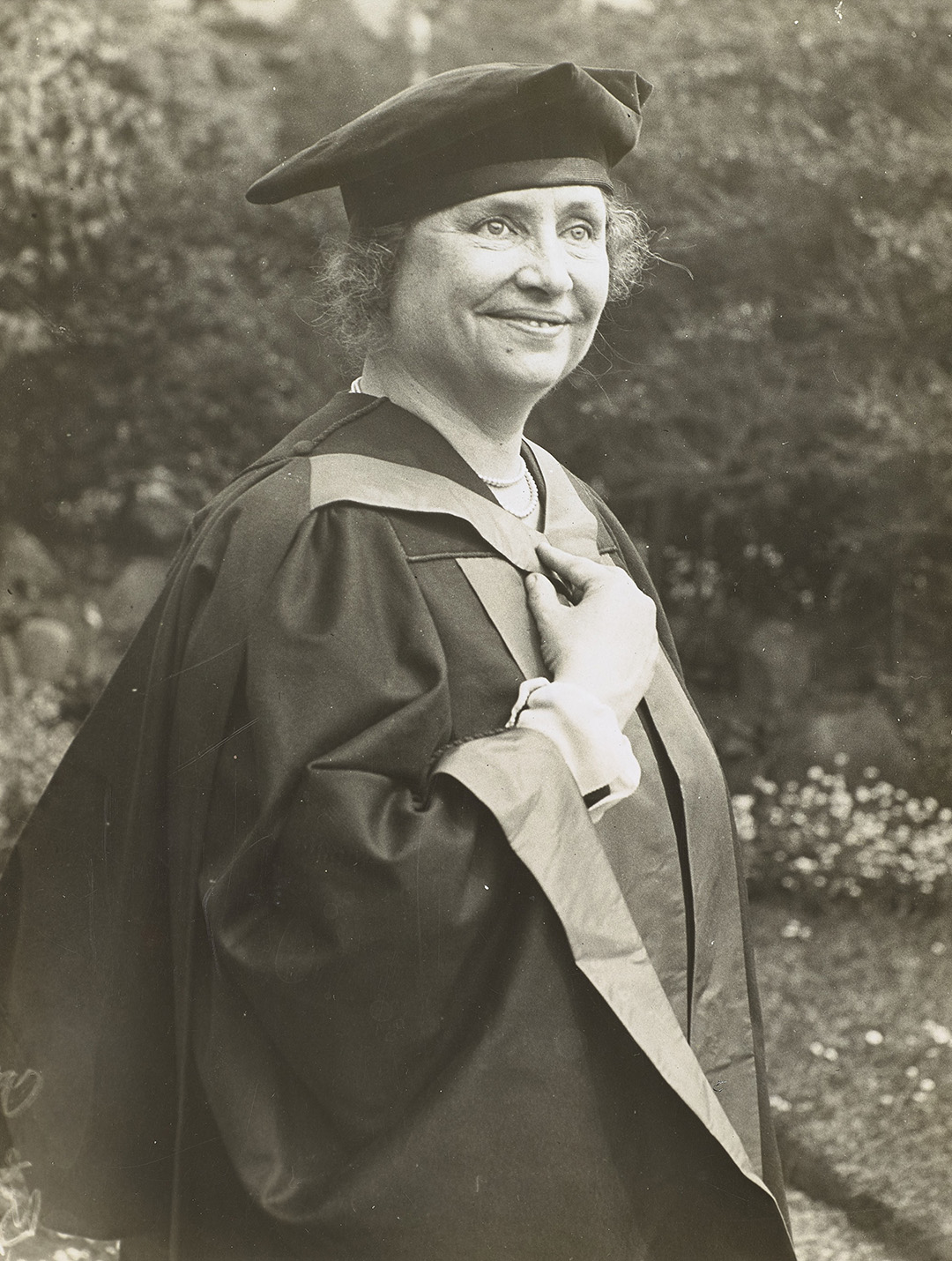 Helen Keller smiling and standing outdoors wearing a cap and gown from Glasgow University.