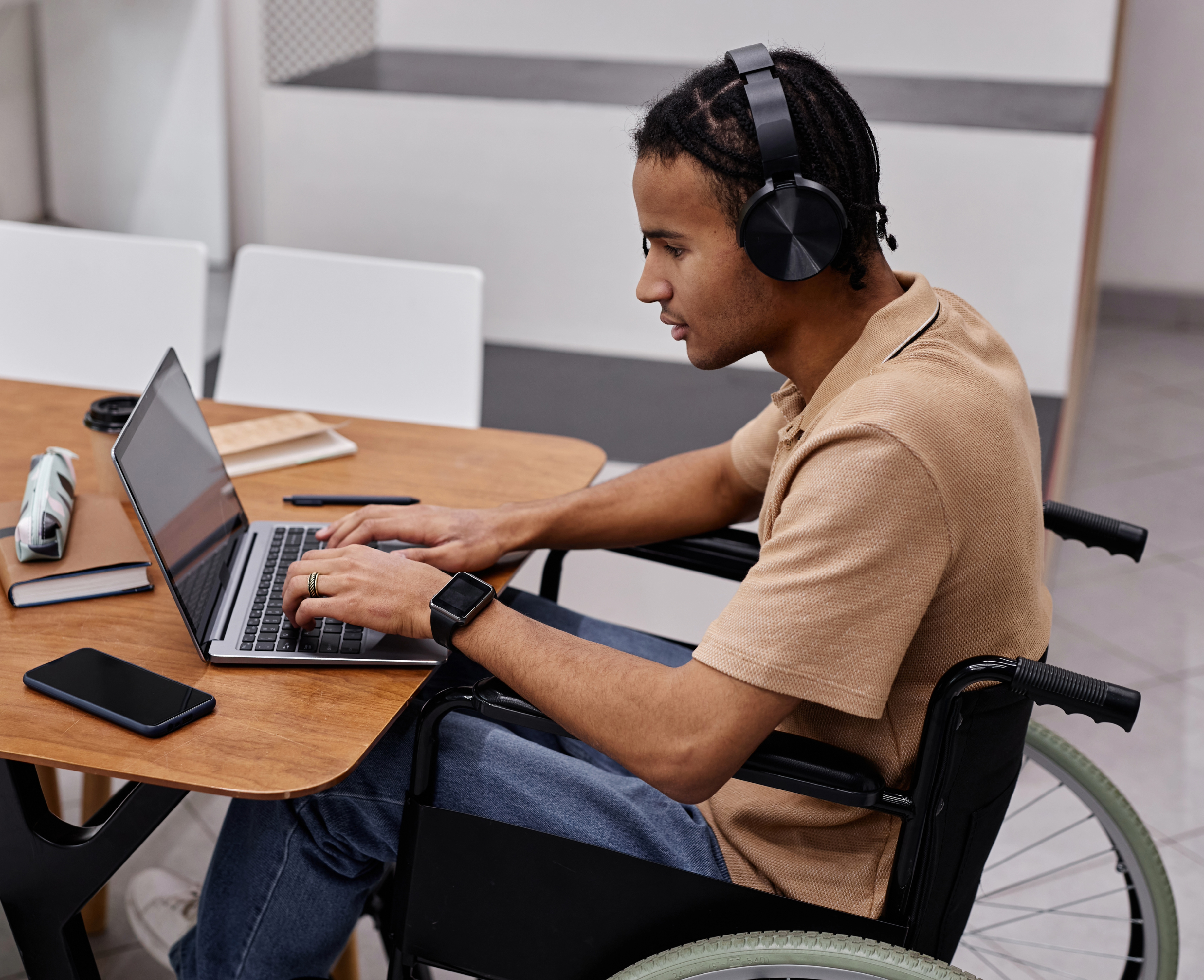 A man in a wheelchair wears headphones while typing on a laptop.