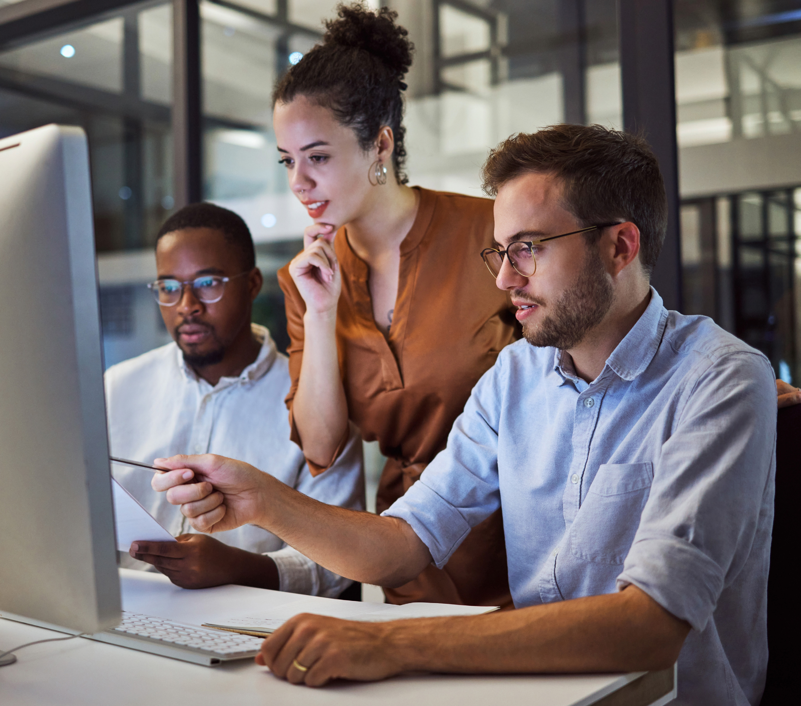 Three coworkers gather around a desktop computer in an office.