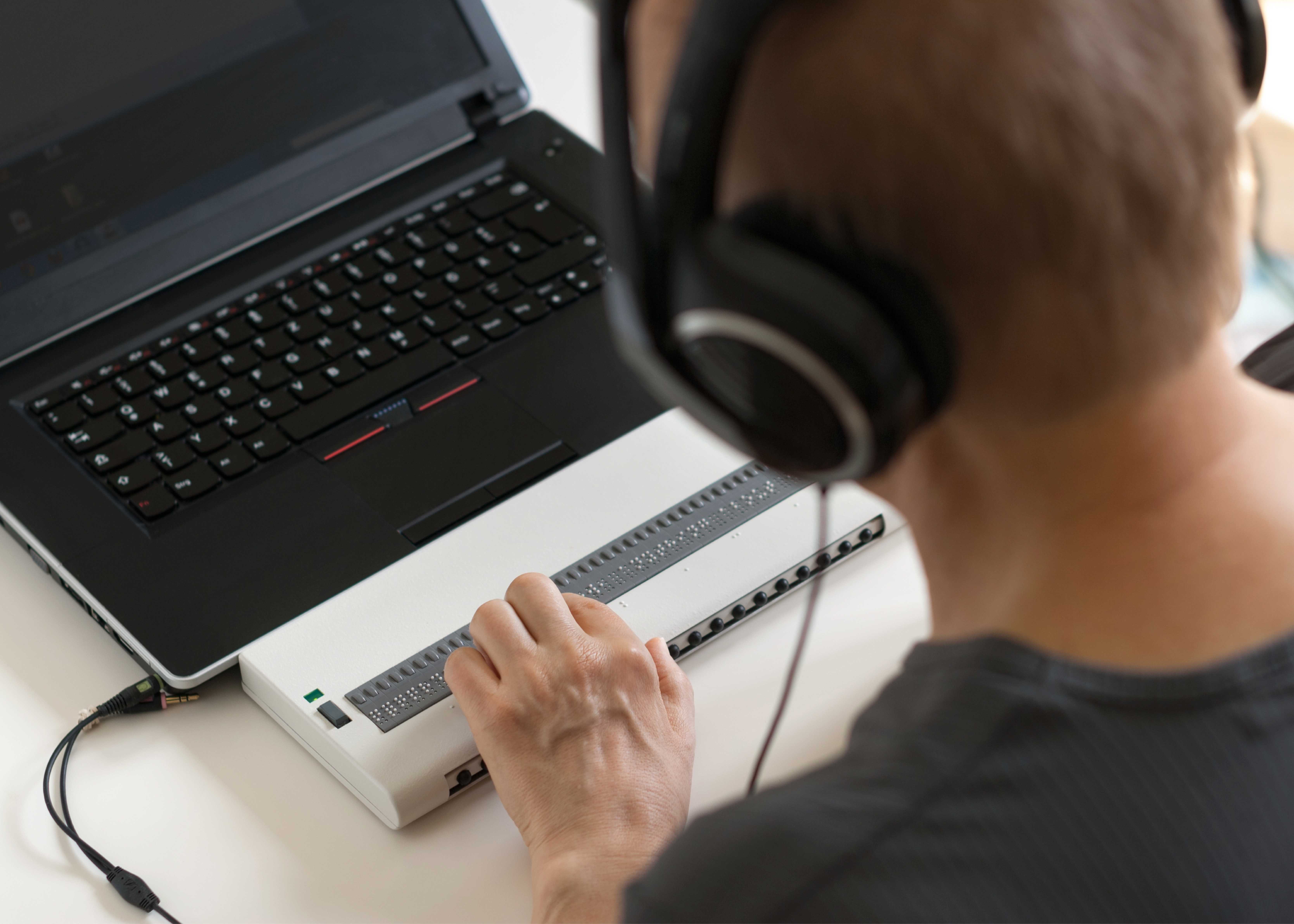 A man wearing headphones uses a braille display.