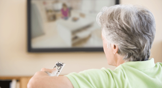 man with white hair watching TV, using remote control