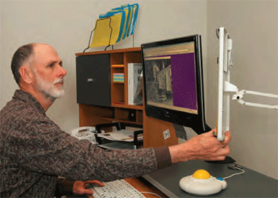 an older man at work reaches out to adjust his large-screen monitor