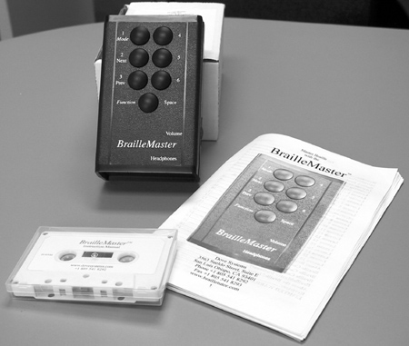 Figure 1: Photograph of the BrailleMaster device, an audiotape, and a printed BrailleMaster manual.