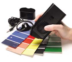 The Speechmaster Colour Detector being held over different color paint chip swatches, with earphone and cover in the background.