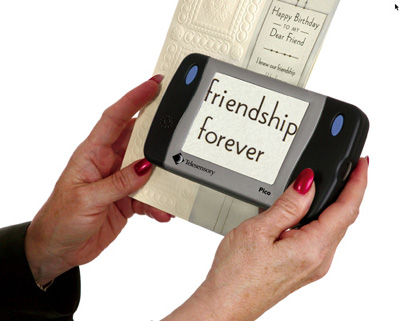 Photo of a woman's hands holding the Pico against a greeting card, which reads "Happy Birthday to my Dear Friend." The Pico's screen displays "friendship forever" in large letters.