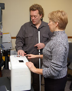 Photo of a man with a long cane and woman examining the bread maker's controls.