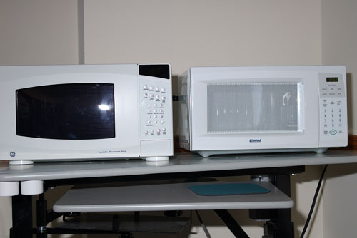 Photo of two microwave ovens side by side. The left one has raised buttons on the control panel, while the right one has a flat screen.