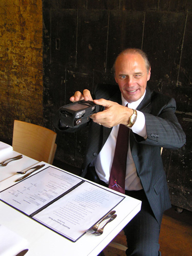 Photo of a smiling Jim Gashel sitting at a table in a restaurant, holding a Reader a few feet above a menu.
