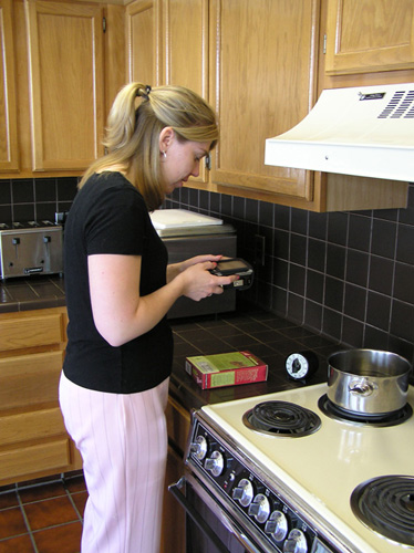 Photo of a woman standing next to a stove using the Reader to read a food package box.