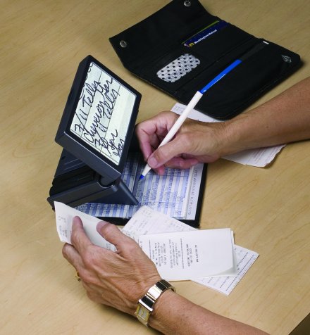 Photo of the Amigo on a writing stand being used to complete entries in a checkbook ledger.