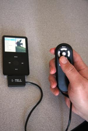 The I-Tell connected by cable to the iPod Classic, while the user's hand operates the remote control.