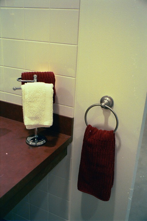 Dark red bathroom towels hang on a white wall, and a white towel contrast with a red countertop.