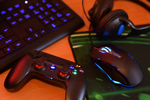 on a table are a gaming joystick controller, mouse, keyboard, and headphones representing the different type of game controls available.