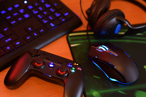 on a table are a gaming joystick controller, mouse, keyboard, and headphones representing the different type of game controls available. 