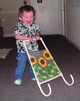 A White toddler pushes an Adaptive Mobility Device in front of him. ” width=“460