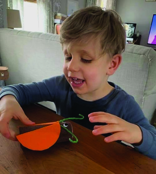 A 4-year old smiling boy sits at a table doing an arts and crafts project.