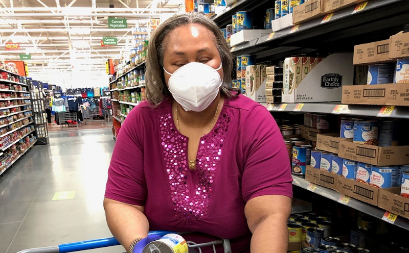 Woman adding canned food to shopping cart in grocery store aisle.