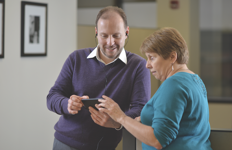 A man wearing earbuds and a woman stand together with a cell phone