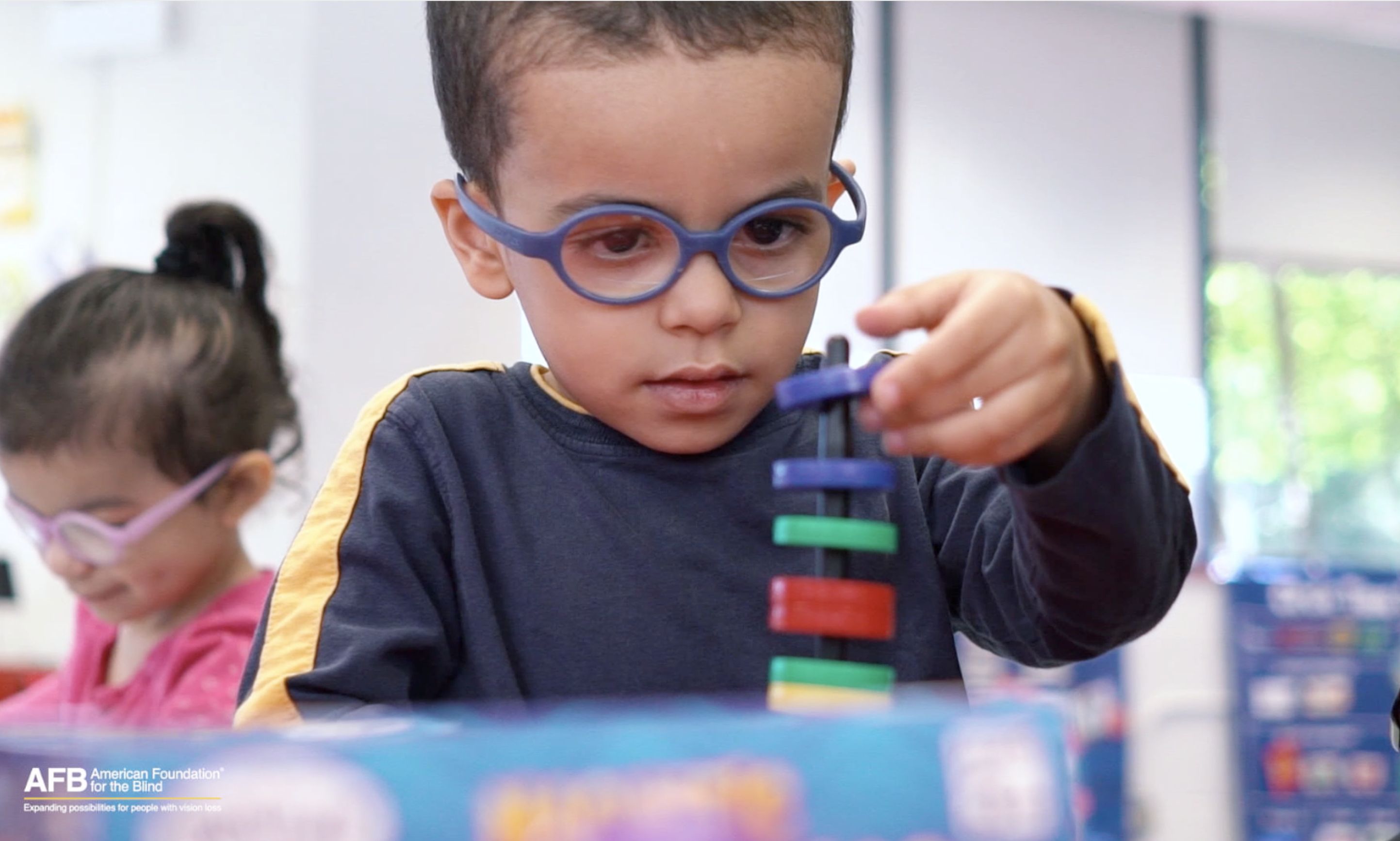 A young boy with a thick-rimmed glasses stares intently at a small ring he is stacking on a toy.