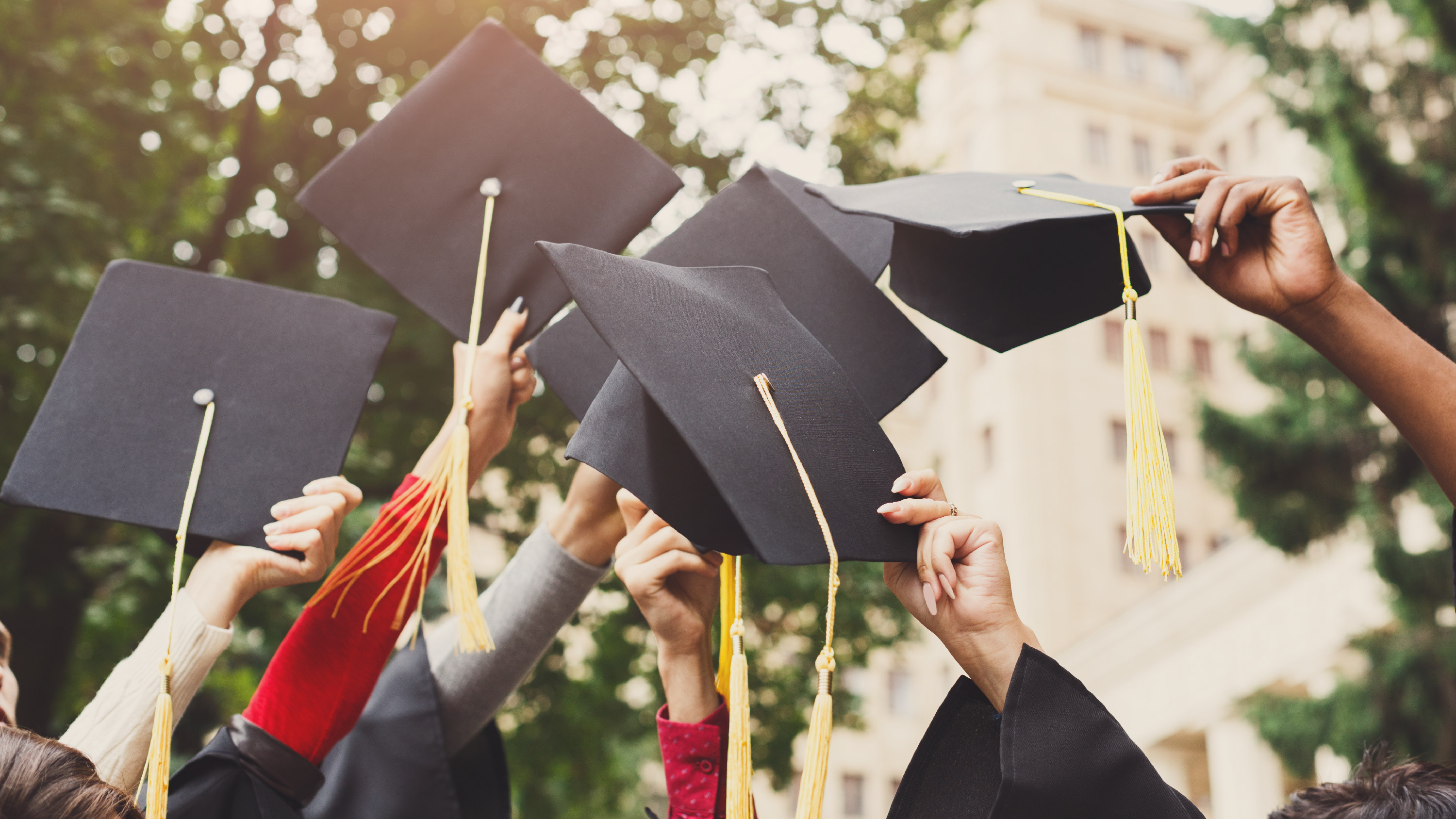 Multiple students raise their graduation caps.