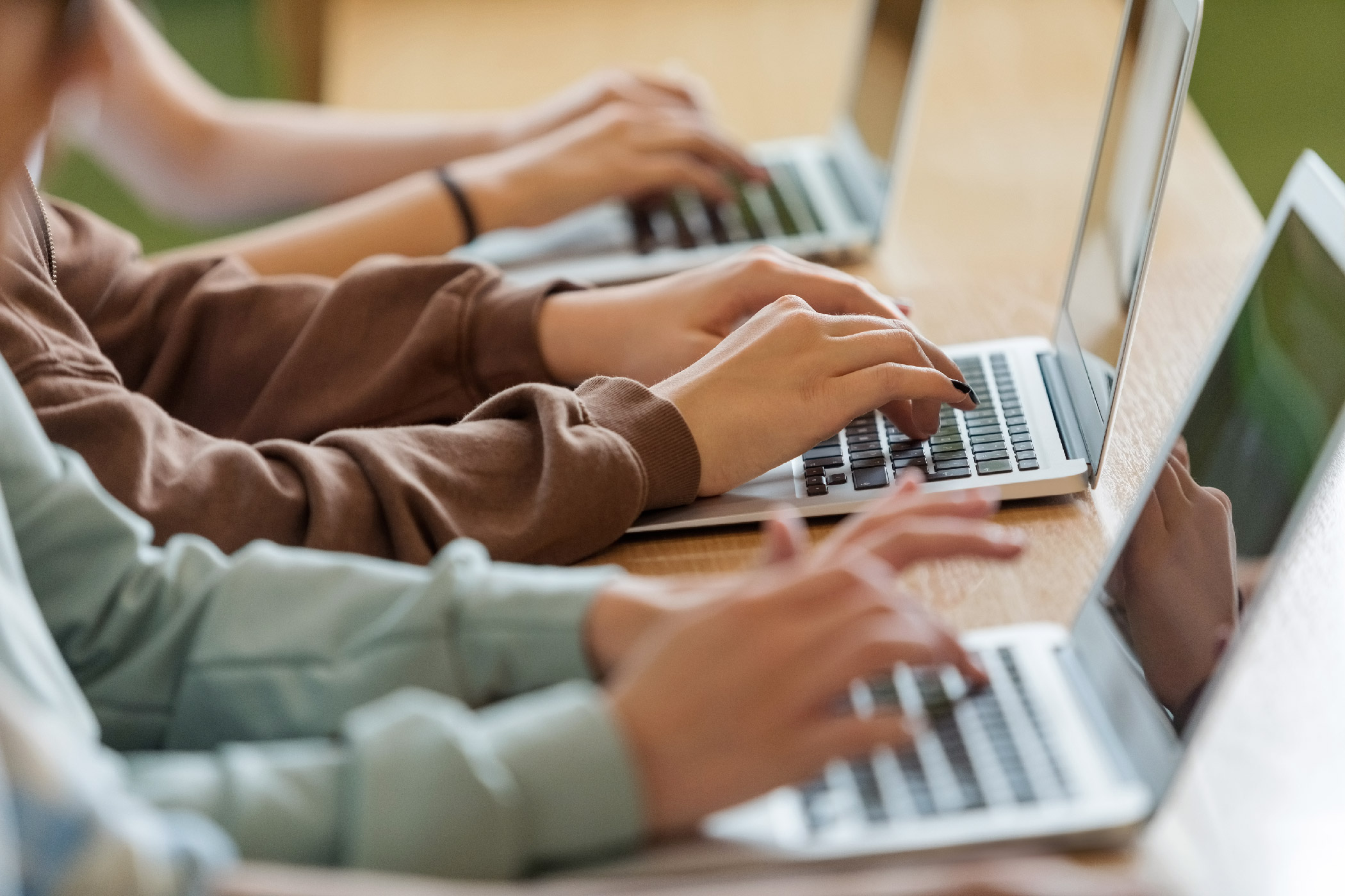 A group of students at a desk working on their laptops.